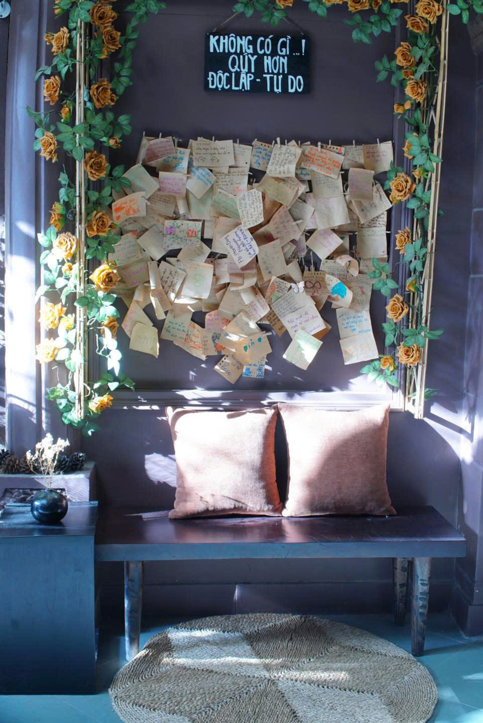 Góc ngồi thư giãn với tường lời nhắn, hoa hồng và ghế gỗ tại Thím's House